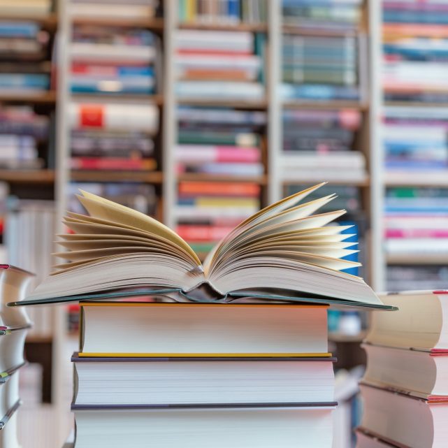 Open novel on stack of books in front of shelf